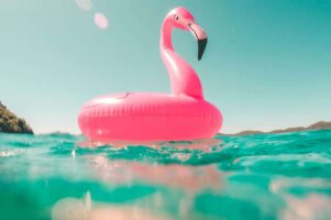 A hot pink flamingo floaty floats in turquoise waters.