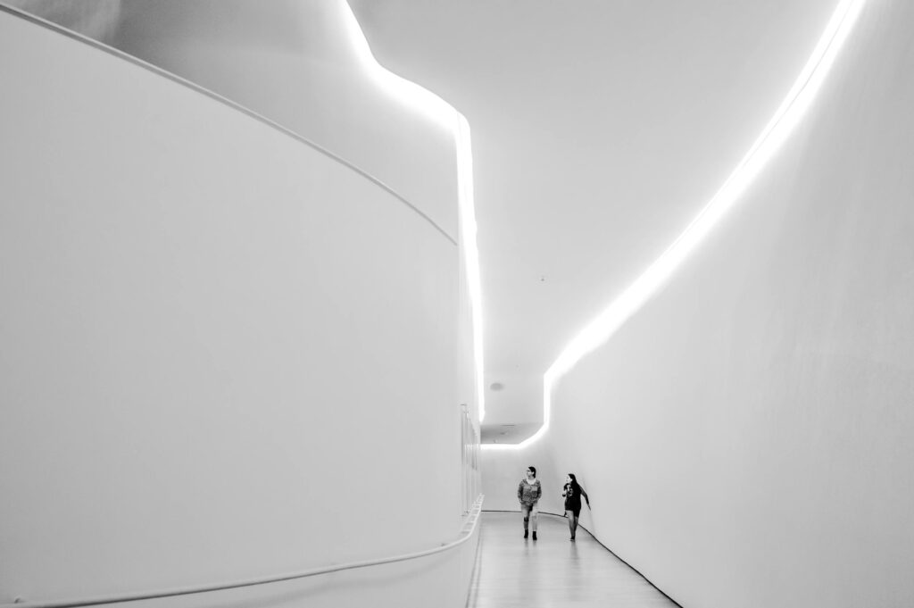 Two people walking in a white futuristic hallway with curved walls and strip lighting
